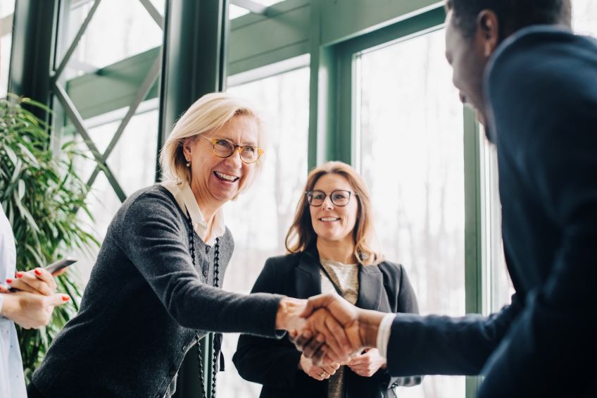 Two businesspeople shaking hands and smiling as two other people look on